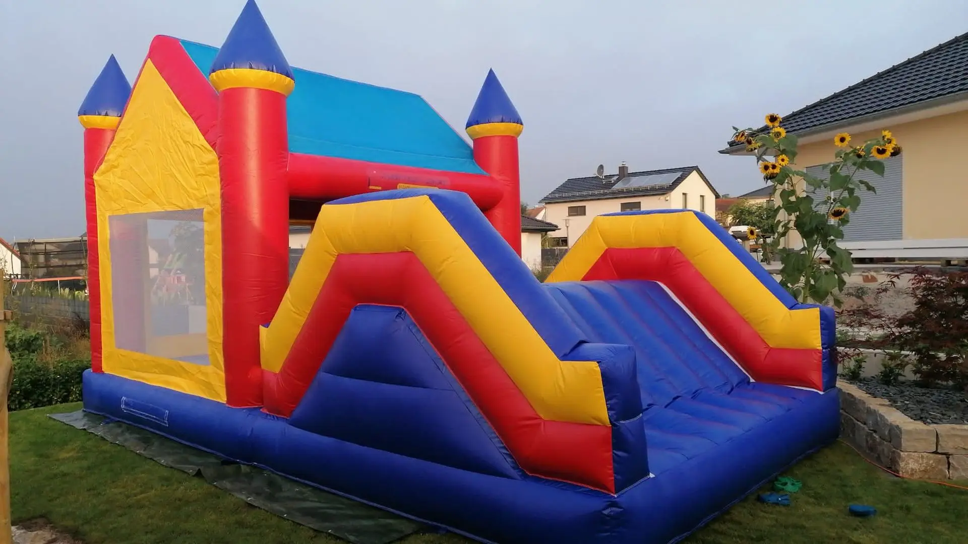 Bunte Hüpfburg mit Rutsche für fröhliche Aktivitäten im Freien! Lebendige Hüpfburg mit Rutsche und leuchtenden Farben, im Garten aufgestellt.