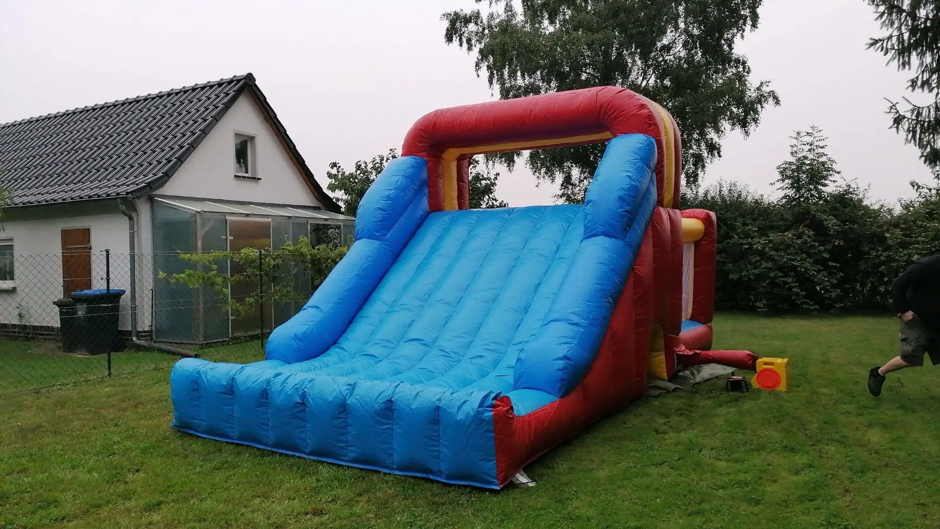 Aufregende Hüpfburg-Rutsche für Spaß im Garten! Große Hüpfburg-Rutsche in leuchtendem Blau und Rot, im Garten aufgestellt.